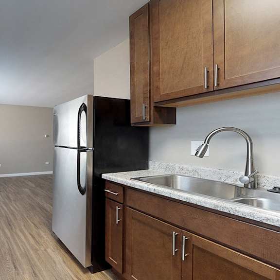 a kitchen with a refrigerator, sink, and wooden cabinets.