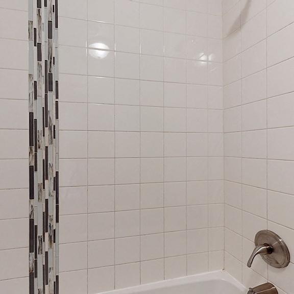 a white tiled shower with a silver faucet.