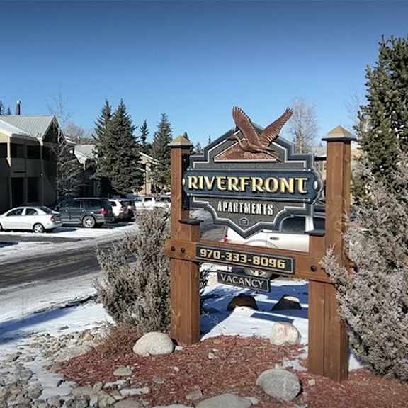 a sign for riverfront apartments stands in front of a building with a car parked in front.