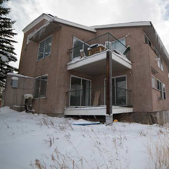 a large brown house with a balcony and snow on the ground.