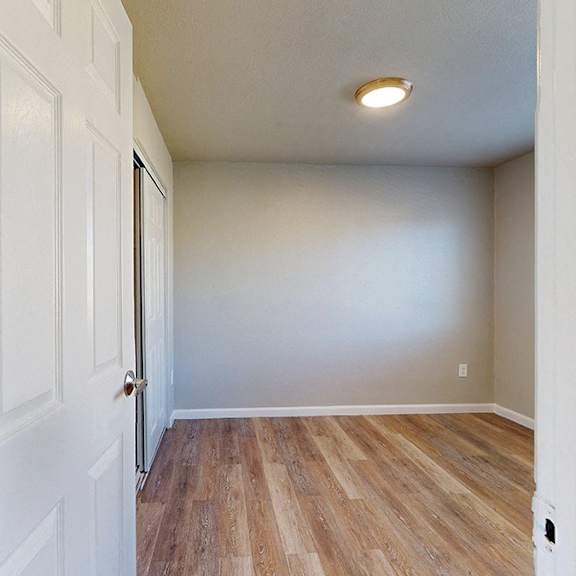 a white door is open to a room with wood flooring.