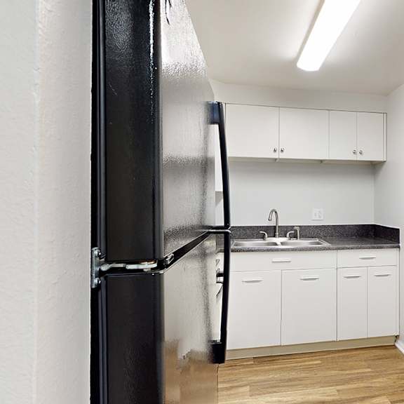 a black refrigerator stands in a kitchen with white cabinets and a black countertop.