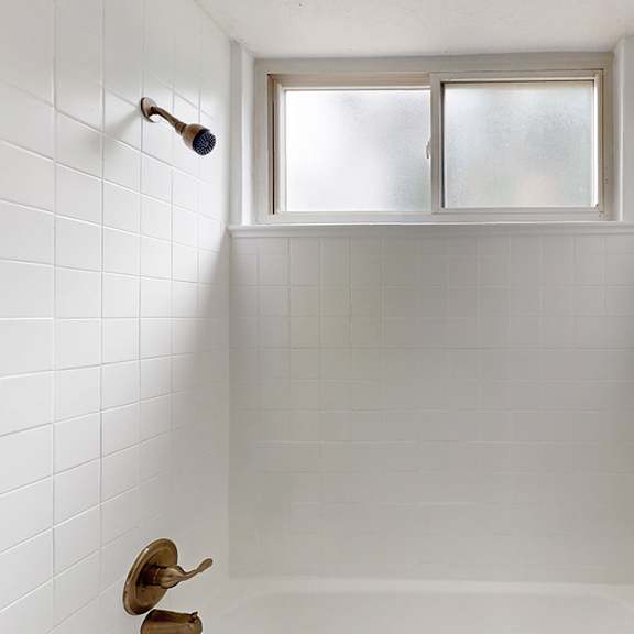 a white tiled bathroom with a window above the bathtub.