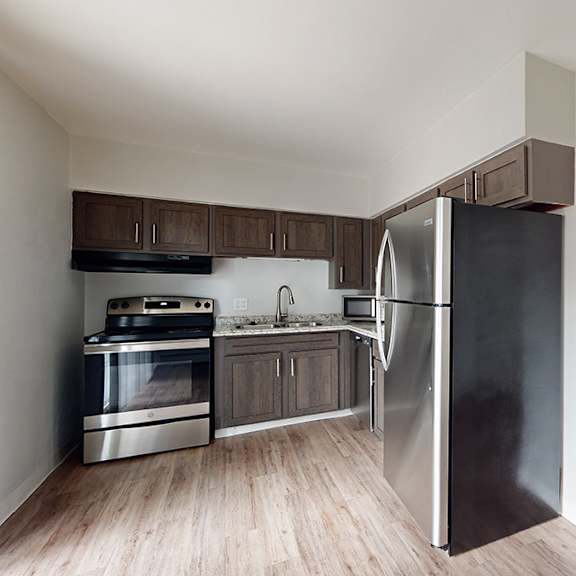 a kitchen with a black refrigerator, stainless steel oven, and wooden cabinets.