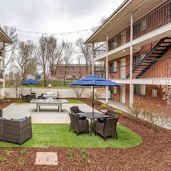 a patio with a table and chairs is surrounded by two buildings.