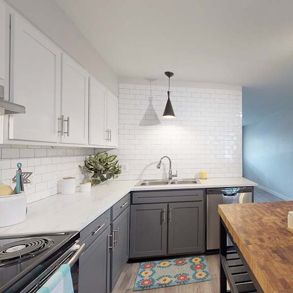 a kitchen with a stove top oven, sink, and a counter with a white pitcher and two cups on it.