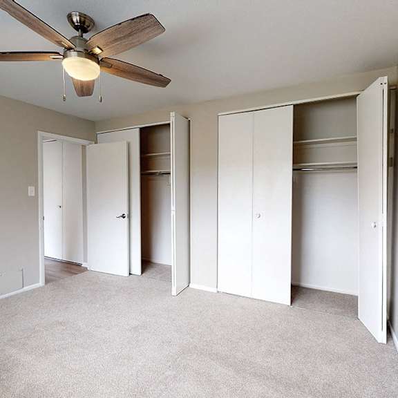 a room with a ceiling fan and three open closets.