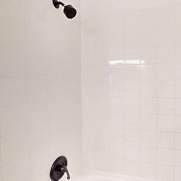 a shower head with a black handle is mounted on a white tiled wall.