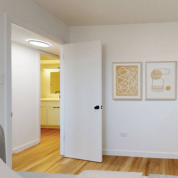 a white interior with a doorway leading to a kitchen and a painting on the wall.