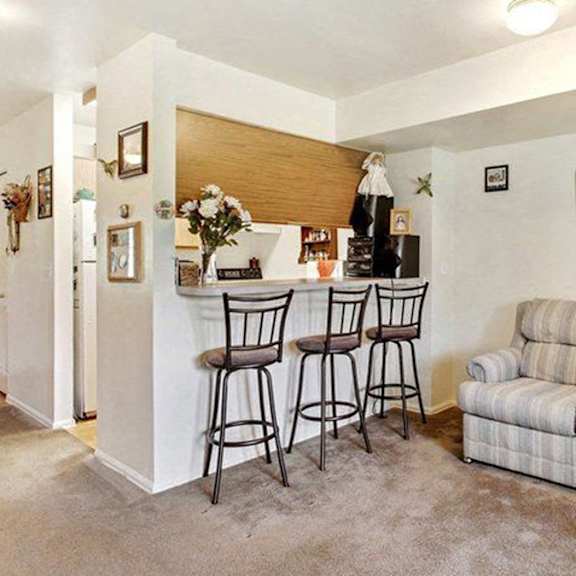 a living room with a couch, bar stools, and a small kitchen area.