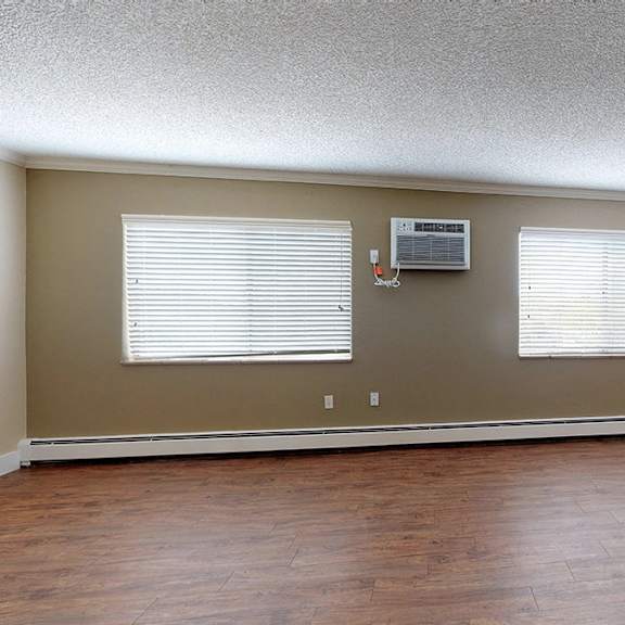 a room with brown floors and a window with blinds.