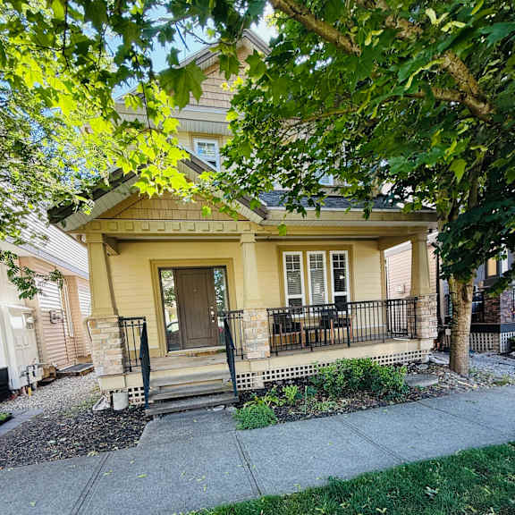 a yellow house with a black fence and a tree in front.