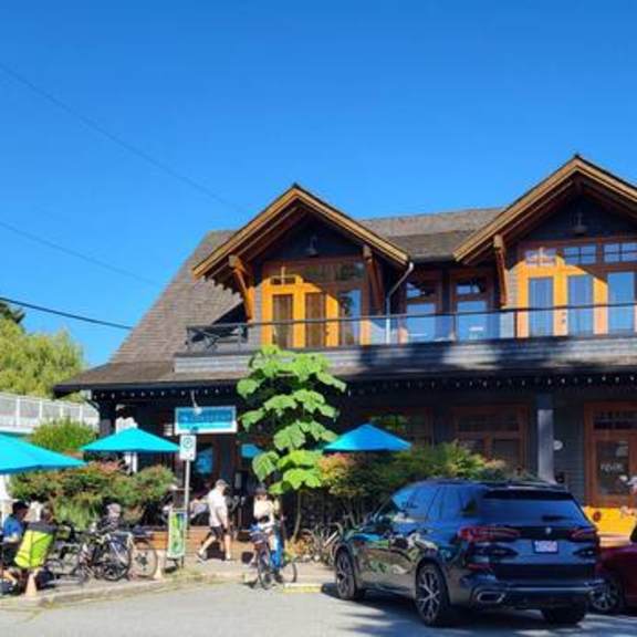a large wooden building with orange trim and a balcony is in the center of a street with people and cars around it.