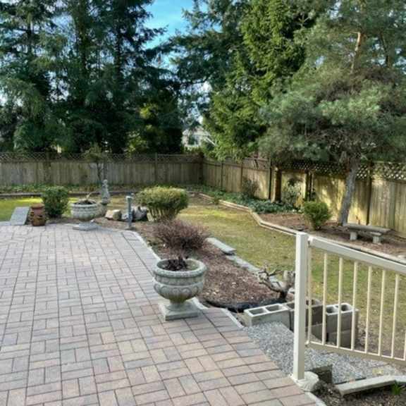 a backyard with a brick walkway and a white fence.