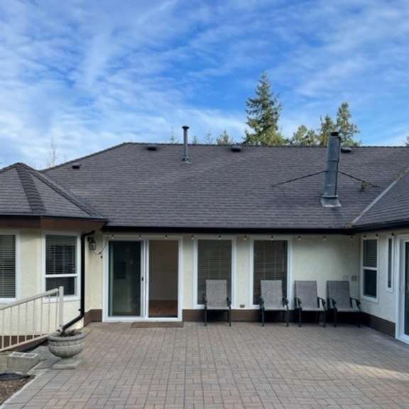 a house with a grey roof and a patio with chairs.