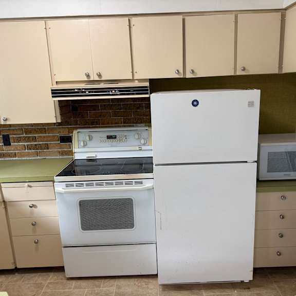 a white refrigerator stands in a kitchen with a brick backsplash.