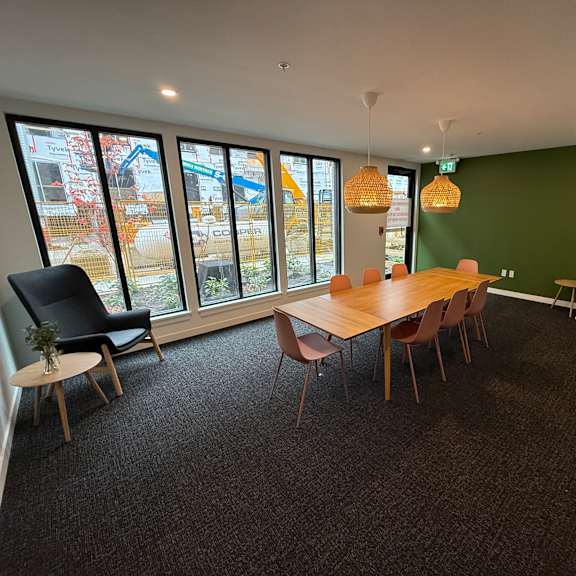 a room with a long table and chairs with a green wall and windows.