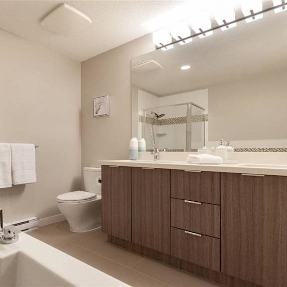 a modern bathroom with a white tub, brown cabinets, and a glass shower enclosure.