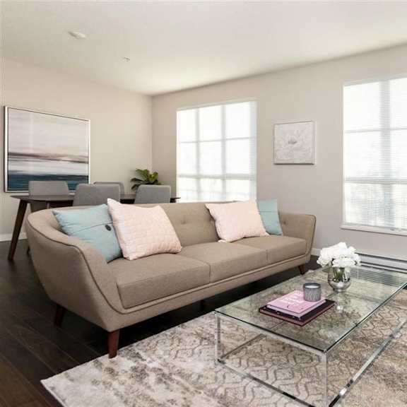a living room with a grey couch, a glass coffee table, and a rug.