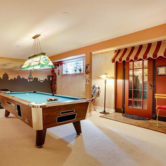 a pool table is in the middle of a room with a green couch and a red chair.