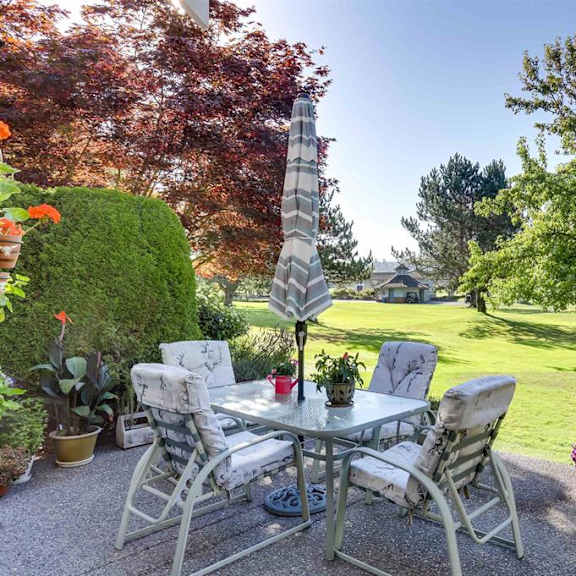 a patio with a table and chairs surrounded by greenery.