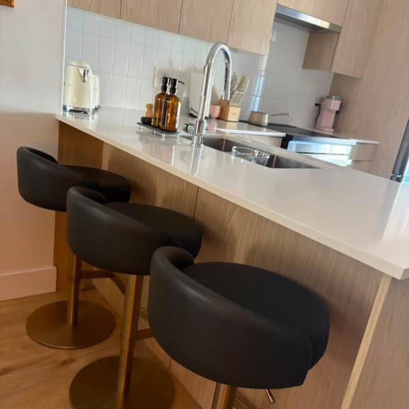 two black bar stools with gold legs in front of a white counter.
