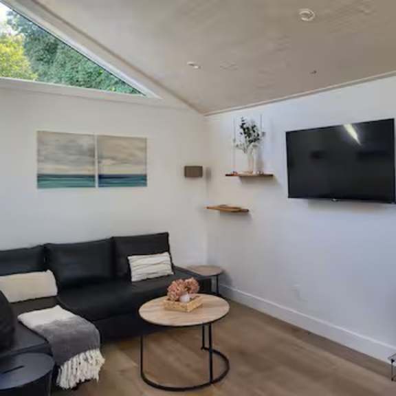 a black couch with a white throw pillow sits in a living room with a flat screen tv mounted on the wall.