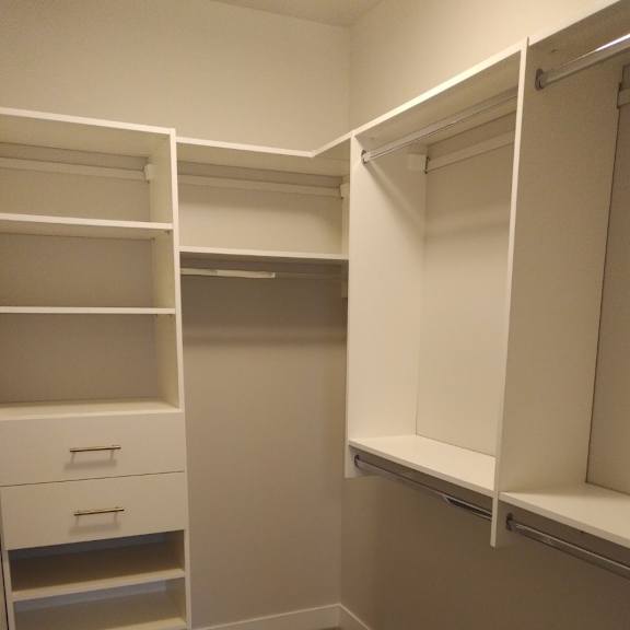 a walk-in closet with white shelving and drawers.