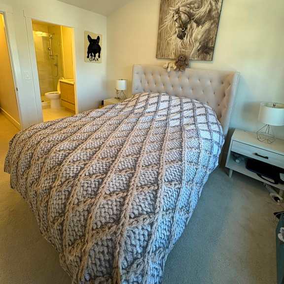 a bed with a white blanket and a white headboard with a painting on the wall.