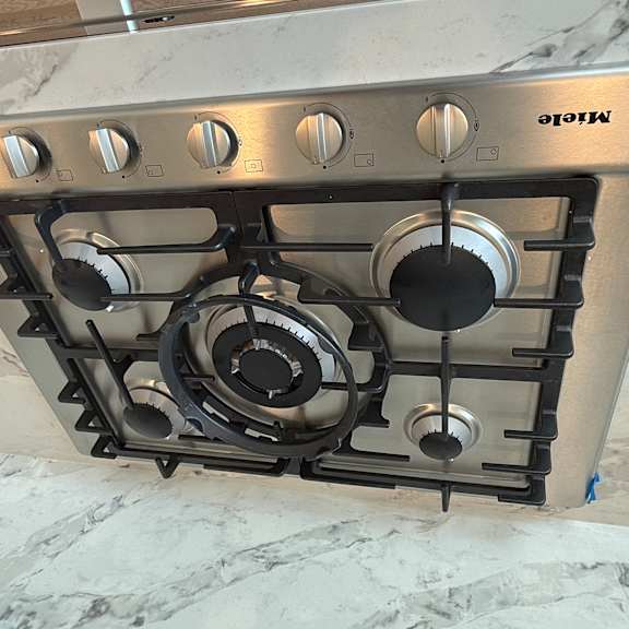 a miele stove top with four burners and a control knob in the center.