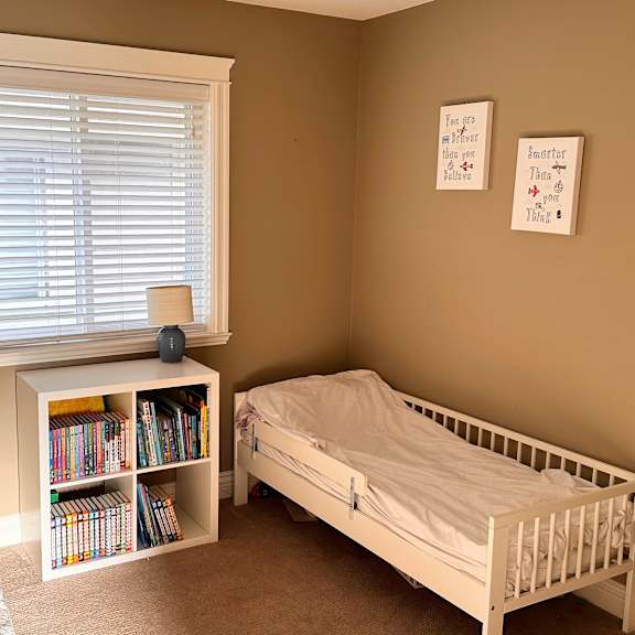 a small child's bedroom with a white bed and a bookshelf.