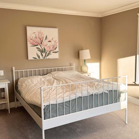 a bedroom with a white bed and a painting of pink flowers on the wall.