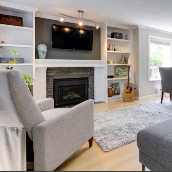 a living room with a grey couch, a grey chair, a grey ottoman, a grey rug, a grey fireplace, a grey wall, a grey floor, a grey ceiling, a grey shelf, a grey cushion