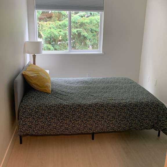 a bed with a yellow pillow and a grey blanket in a room with a window.