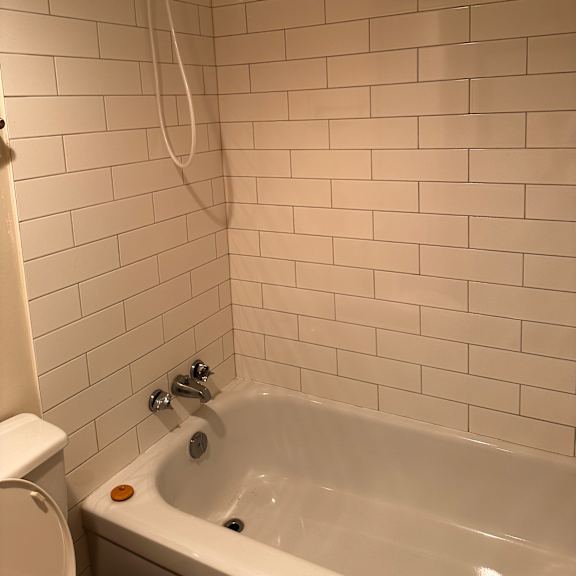 a white tiled bathroom with a shower head and a hose.