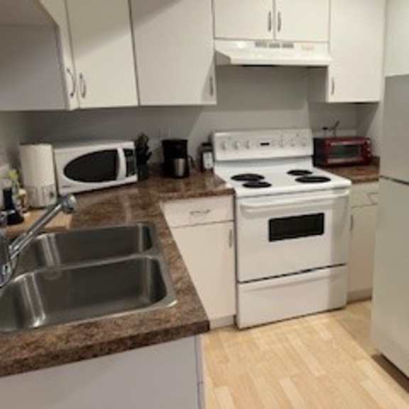 a white kitchen with a stove, sink, and refrigerator.