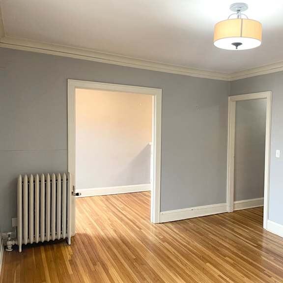a room with a white wall and a wooden floor with a radiator.