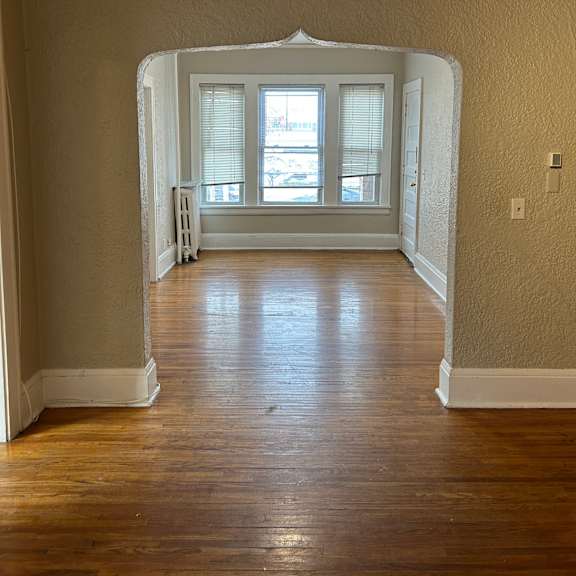 a room with a wooden floor and a white archway leading to a window.