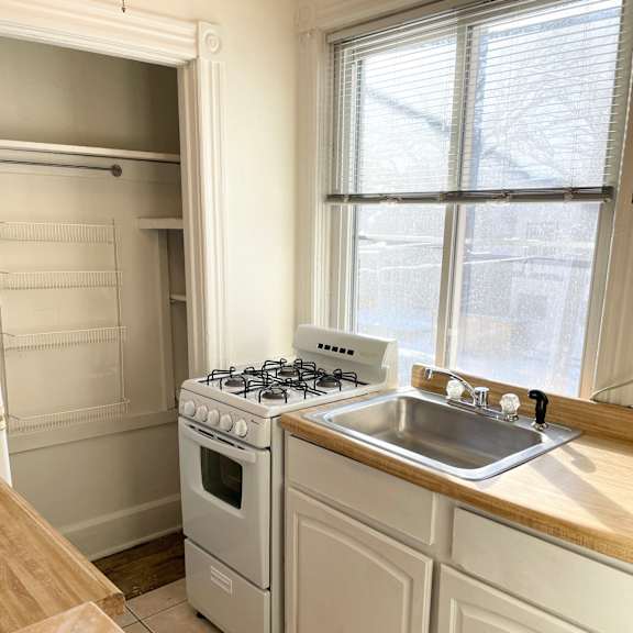 a white kitchen with a stove, sink, and cabinets.
