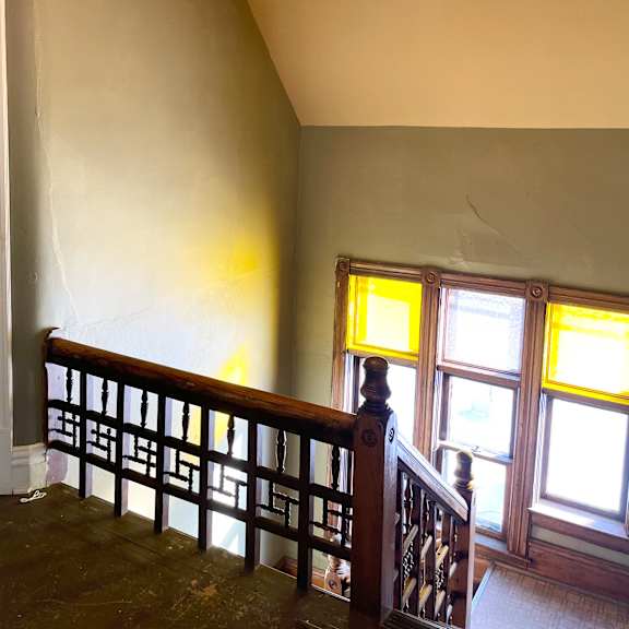 a chandelier hangs from the ceiling in a room with a wooden staircase.