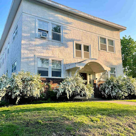 a house with a white and beige exterior and a green lawn in front.