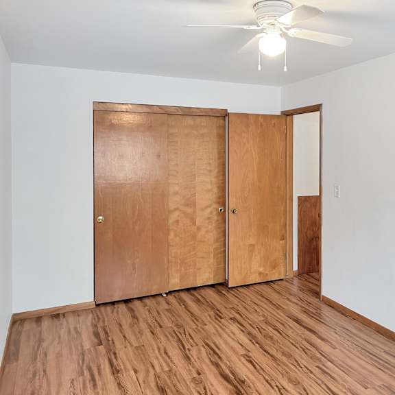 a room with a ceiling fan and a wooden floor with two doors.
