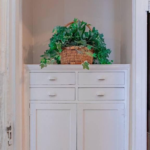 a white cabinet with a basket of green plants on top.