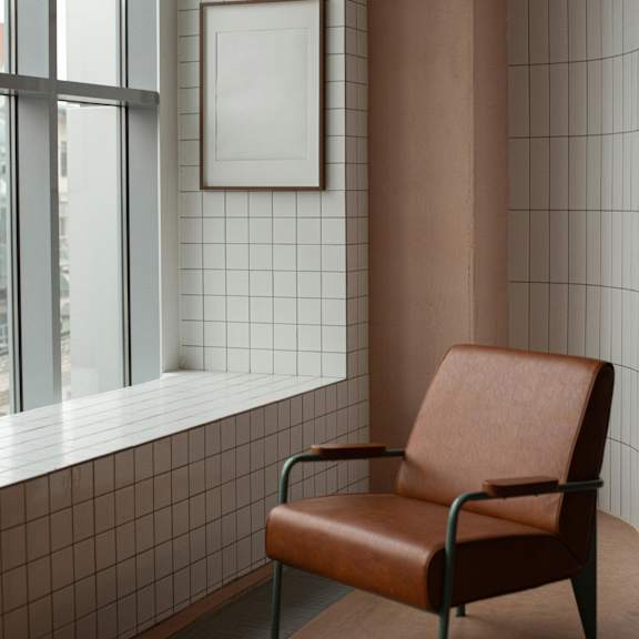 a brown leather chair sits in front of a window with a white frame and a picture on the wall.