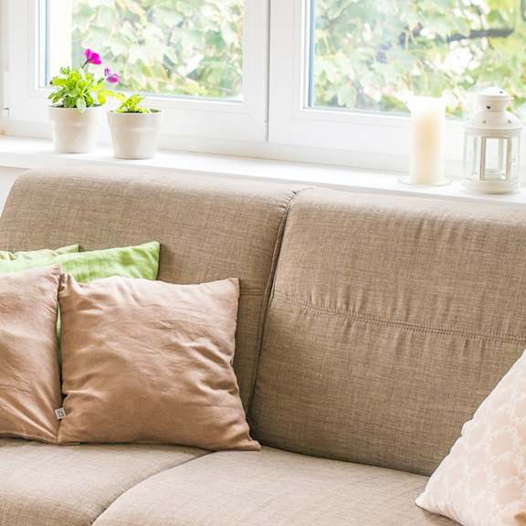 a beige couch with two pillows and a small table with a lamp on it.