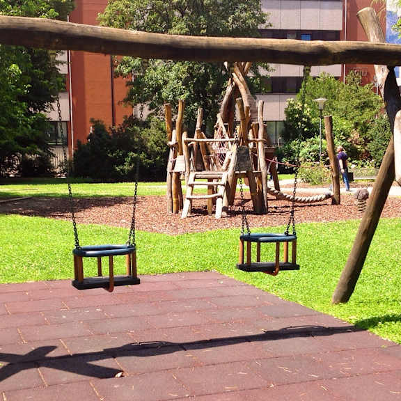 a swing set in a park with a red brick building in the background.
