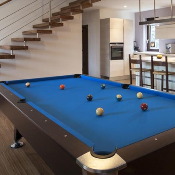 a pool table is in the middle of a room with a staircase.