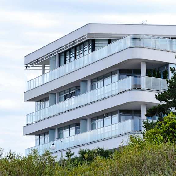 a white building with balconies is surrounded by greenery.