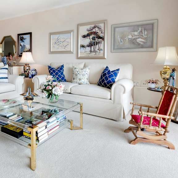 a living room with a white couch, a glass coffee table, and a wooden rocking chair.