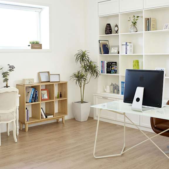 a white desk with a computer and a chair in front of a window with a shelf and potted plant.
